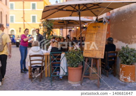 Busy outdoor street cafe terrace with people dining and big wooden menu board. 140681647