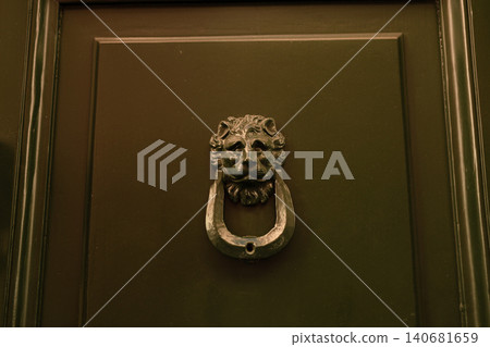 Vintage brass lion head door knocker on a dark green wooden door panel. 140681659