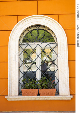 Beautiful arched window with decorative wrought iron grate on vibrant orange wall Mediterranean style building exterior. Beautiful arched window with decorative wrought iron grate on vibrant orange wall Mediterranean style building exterior. 140681667