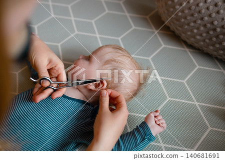 Close-up of a mother carefully trimming her baby son's hair with scissors Close-up of a mother carefully trimming her baby son's hair with scissors 140681691