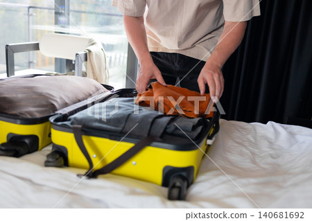 Packing clothes into yellow suitcase on bed travel preparation Packing clothes into yellow suitcase on bed travel preparation 140681692