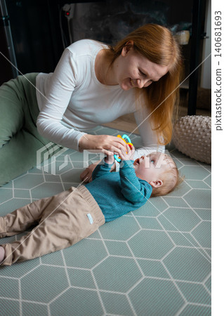 Happy mother playing with her infant baby boy on the floor at home Happy mother playing with her infant baby boy on the floor at home 140681693