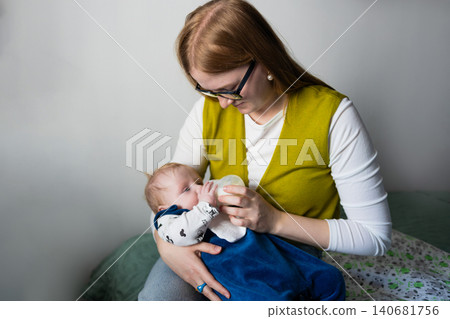 Portrait of a happy smiling mother bottle-feeding her infant baby at home. Portrait of a happy smiling mother bottle-feeding her infant baby at home. 140681756