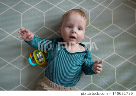 Adorable baby lying on soft play mat and playing with colorful toy, top view perspective, early development, curiosity and parenting concept. Adorable baby lying on soft play mat and playing with colorful toy, top view perspective, early development, curiosity and parenting concept. 140681759