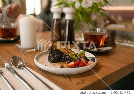 Slice of chocolate cake served with fresh berries and tea on wooden table in cozy cafe environment with soft natural light. Slice of chocolate cake served with fresh berries and tea on wooden table in cozy cafe environment with soft natural light. 140681771
