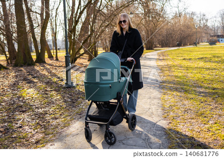 30s mother woman walking along park path while pushing baby stroller, enjoying sunny day and outdoor parenting lifestyle. 30s mother woman walking along park path while pushing baby stroller, enjoying sunny day and outdoor parenting lifestyle. 140681776