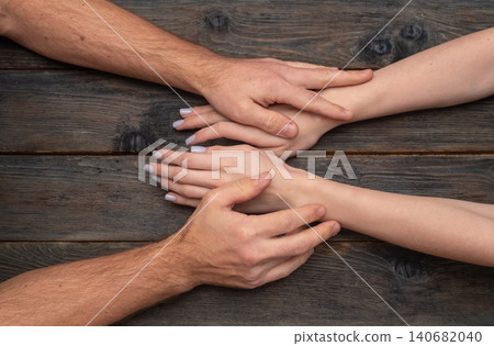 Male and female hands touch gently on dark rustic wooden table showing love. Tender palms express romantic bond and emotional support between partners. Hands symbolize trust and care in intimate Male and female hands touch gently on dark rustic wooden table showing love. Tender palms express romantic bond and emotional support between partners. Hands symbolize trust and care in intimate 140682040