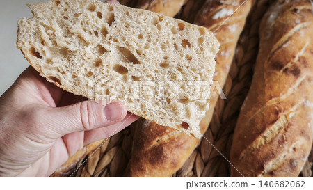 baguette piece held in hand showing porous crumb texture against background of whole bread. baguette piece held in hand showing porous crumb texture against background of whole bread. 140682062