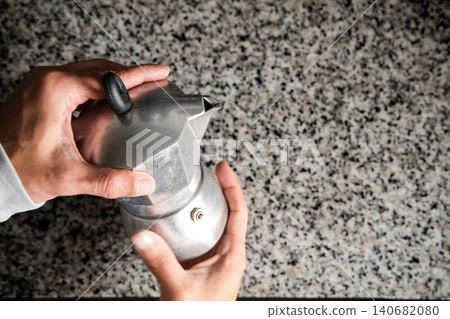 A person is holding a silver coffee pot with a lid on it A person is holding a silver coffee pot with a lid on it 140682080