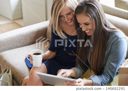 Women, coffee and happy on sofa with tablet for streaming, ecommerce or watching video together in living room. Female people, smile and technology for friendship, bonding and social media in home Women, coffee and happy on sofa with tablet for streaming, ecommerce or watching video together in living room. Female people, smile and technology for friendship, bonding and social media in home 140682291