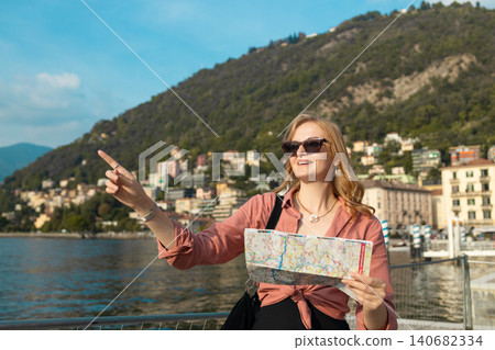 Happy blonde woman traveler searching for direction with city map against mountain lake Happy blonde woman traveler searching for direction with city map against mountain lake 140682334