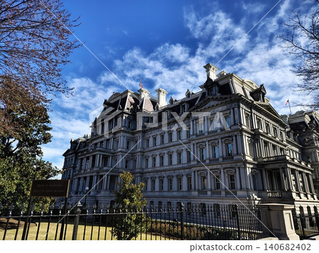 A side view of the Dwight D. Eisenhower Executive Office Building, empty of people, on a bright sunny day, framed by park trees. A side view of the Dwight D. Eisenhower Executive Office Building, empty of people, on a bright sunny day, framed by park trees. 140682402