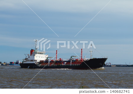 Tanker ship cargo river harbor port industry transport, black and white vessel cruising past industrial terminal under blue sky, maritime logistics and fuel delivery concept 140682741