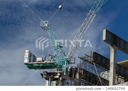 Tower crane construction site steel beam scaffolding blue sky cloud lifting infrastructure, heavy equipment working above building frame, safety lighting, urban development under daylight Tower crane construction site steel beam scaffolding blue sky cloud lifting infrastructure, heavy equipment working above building frame, safety lighting, urban development under daylight 140682749