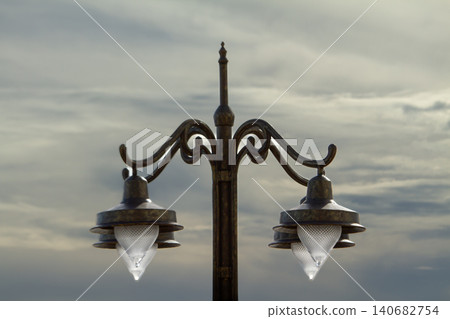 Streetlight lamp lantern metal vintage ornate pole sky, twin outdoor light fixture with wrought iron scrollwork against cloudy evening horizon, urban lighting detail Streetlight lamp lantern metal vintage ornate pole sky, twin outdoor light fixture with wrought iron scrollwork against cloudy evening horizon, urban lighting detail 140682754