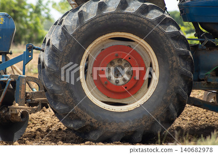 Tractor wheel tire agriculture farm field soil machinery closeup of rugged tread and rim on working vehicle during plowing, dusty ground and rural landscape in daylight Tractor wheel tire agriculture farm field soil machinery closeup of rugged tread and rim on working vehicle during plowing, dusty ground and rural landscape in daylight 140682978