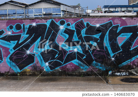 Graffiti mural on wall in urban street with abstract black and blue paint, public art on concrete barrier Graffiti mural on wall in urban street with abstract black and blue paint, public art on concrete barrier 140683070