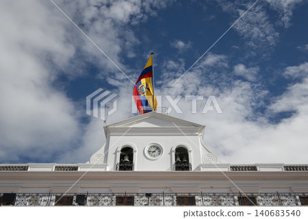 Front facade of the Carondelet Palace, seat of the Ecuadorian government, with a tricolor flag waving in the wind against a blue sk Front facade of the Carondelet Palace, seat of the Ecuadorian government, with a tricolor flag waving in the wind against a blue sk 140683540