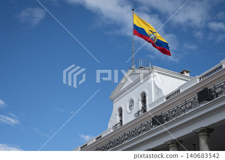 An angled view of the white facade and colonnade of the historic Carondelet Palace, the presidential residence, with the national flag waving under a blue sky in Quito, Ecuador. An angled view of the white facade and colonnade of the historic Carondelet Palace, the presidential residence, with the national flag waving under a blue sky in Quito, Ecuador. 140683542