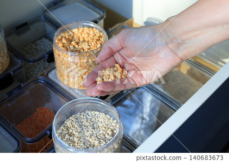Woman hand holding yellow split peas over pantry containers, kitchen drawer storage with dry grains and legumes close up Woman hand holding yellow split peas over pantry containers, kitchen drawer storage with dry grains and legumes close up 140683673