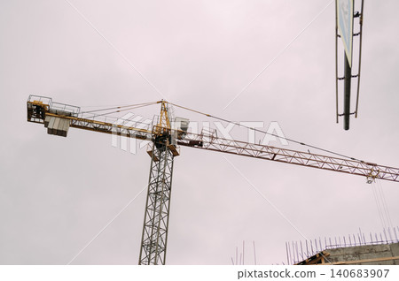 Tower crane at construction site against overcast sky Tower crane at construction site against overcast sky 140683907