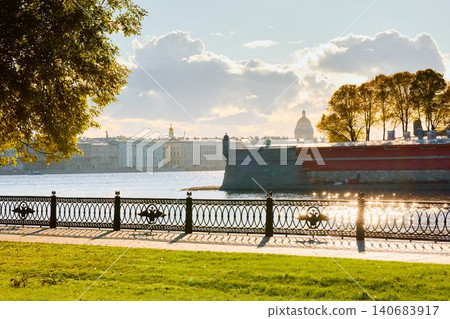 Isaac cathedral, Winter Palace, picturesque metal railings with a double-headed eagle and the crown of the Russian Empire on embankment in St. Petersburg, autumn sunset, incredible sun glare, Russia 140683917