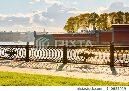 Isaac cathedral, Winter Palace, picturesque metal railings with a double-headed eagle and the crown of the Russian Empire on embankment in St. Petersburg, autumn sunset, incredible sun glare, Russia Isaac cathedral, Winter Palace, picturesque metal railings with a double-headed eagle and the crown of the Russian Empire on embankment in St. Petersburg, autumn sunset, incredible sun glare, Russia 140683919