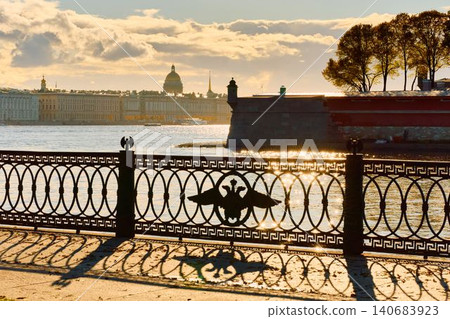 Isaac cathedral, Winter Palace, picturesque metal railings with a double-headed eagle and the crown of the Russian Empire on embankment in St. Petersburg, autumn sunset, incredible sun glare, Russia Isaac cathedral, Winter Palace, picturesque metal railings with a double-headed eagle and the crown of the Russian Empire on embankment in St. Petersburg, autumn sunset, incredible sun glare, Russia 140683923