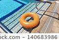 An inflatable orange float on a hotel pool deck, the float lies on a tiled surface with steps leading into the water by the pool in summer. 140683986