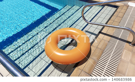 An inflatable orange float on a hotel pool deck, the float lies on a tiled surface with steps leading into the water by the pool in summer. An inflatable orange float on a hotel pool deck, the float lies on a tiled surface with steps leading into the water by the pool in summer. 140683986