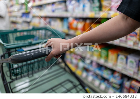A woman's hands pushing a shopping cart in the supermarket aisle. A woman's hands pushing a shopping cart in the supermarket aisle. 140684338