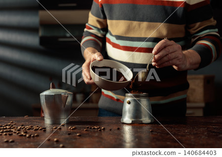 A man in a striped jumper is about to make coffee in an old Italian coffee maker. A man in a striped jumper is about to make coffee in an old Italian coffee maker. 140684403
