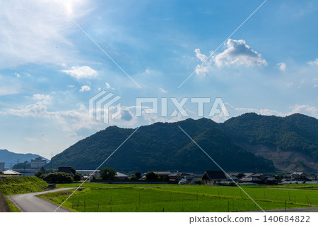 A Japanese rural landscape unfolds against a backdrop of blue skies and mountain ranges. A Japanese rural landscape unfolds against a backdrop of blue skies and mountain ranges. 140684822