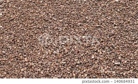 A close view of a dense ground surface covered with small pebbles and mixed stones in brown and gray tones, creating a rough natural texture with even daylight and a uniform A close view of a dense ground surface covered with small pebbles and mixed stones in brown and gray tones, creating a rough natural texture with even daylight and a uniform 140684931