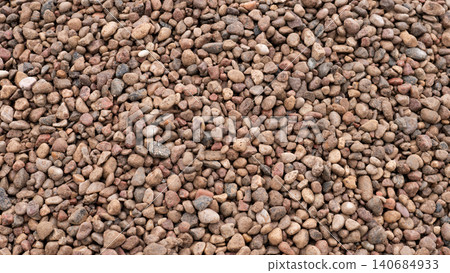 A close view of many small natural stones and pebbles forming a rough gravel surface with mixed beige, brown, gray, and tan tones under even daylight A close view of many small natural stones and pebbles forming a rough gravel surface with mixed beige, brown, gray, and tan tones under even daylight 140684933