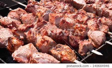 Close view of thick pieces of meat cooking on metal skewers over hot charcoal, with browned surfaces, roasted texture, and visible smoke-free high heat in an outdoor grilling setup 140684946