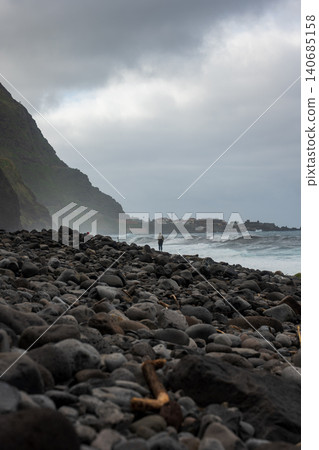 Person on basalt beach below cliffs, Madeira, Portugal, Atlantic surf 140685158