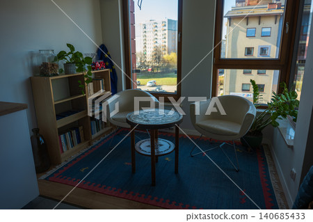 Modern apartment reading nook with cream armchairs and blue rug Modern apartment reading nook with cream armchairs and blue rug 140685433