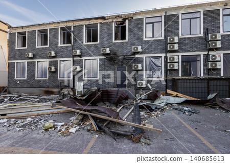 Bila Tserkva, Kyiv region, Ukraine - 09.06.2025: Facade of damaged two story grey brick building with shattered windows covered in plastic many air conditioners and roof debris on street after blast Bila Tserkva, Kyiv region, Ukraine - 09.06.2025: Facade of damaged two story grey brick building with shattered windows covered in plastic many air conditioners and roof debris on street after blast 140685613