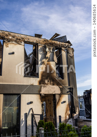Bila Tserkva, Kyiv region, Ukraine - 09.06.2025: Modern residential house completely ruined after fire explosion with collapsed roof charred walls and empty shattered window frames against blue sky 140685614