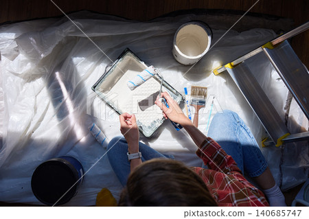 Overhead view of person holding paint roller above tray with bucket, brushes and ladder on protective sheet Overhead view of person holding paint roller above tray with bucket, brushes and ladder on protective sheet 140685747