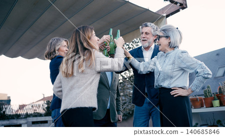 Group of friends celebrating on a rooftop terrace, toasting with beer bottles Group of friends celebrating on a rooftop terrace, toasting with beer bottles 140685846
