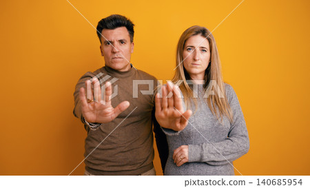 Couple showing stop gesture standing on orange background Couple showing stop gesture standing on orange background 140685954