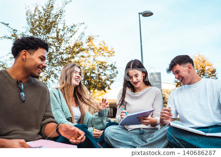 Diverse university students laughing, studying together outdoors 140686287