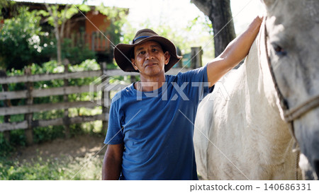 Latino stableman standing with his white horse on a ranch 140686331