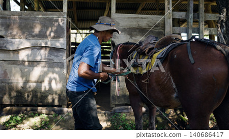 Latino man saddling a horse near a stable 140686417