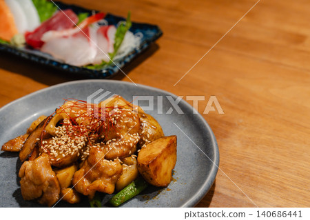 日式料理，如刺身和炒雞肉，擺放在木桌上，風格類似居酒屋（日本酒吧）。 140686441