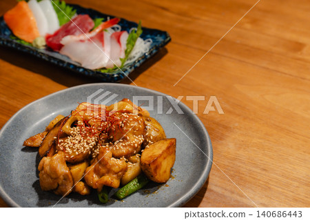 雞肉地瓜炒菜和一盤生魚片,全部擺在居酒屋(日本酒吧)的桌上。 雞肉地瓜炒菜和一盤生魚片,全部擺在居酒屋(日本酒吧)的桌上。 140686443