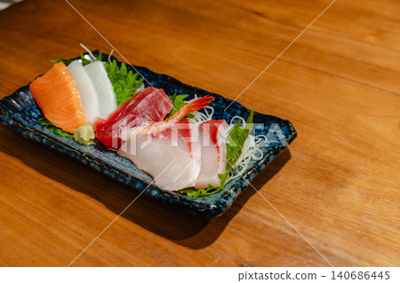 Enjoy a platter of fresh sashimi at a wooden table in an izakaya (Japanese pub). Enjoy a platter of fresh sashimi at a wooden table in an izakaya (Japanese pub). 140686445