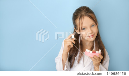 A girl in a medical gown with a jaw model in her hands demonstrates a missing tooth. World Dental and Oral Hygiene Day A girl in a medical gown with a jaw model in her hands demonstrates a missing tooth. World Dental and Oral Hygiene Day 140686456